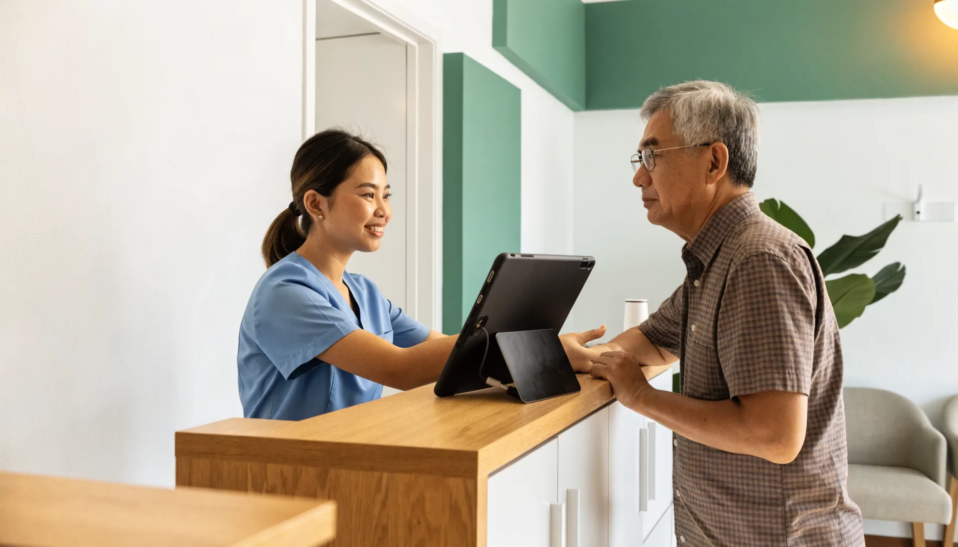 The receptionist welcomes an arriving patient at the clinic’s front desk, the waiting area calm behind him.