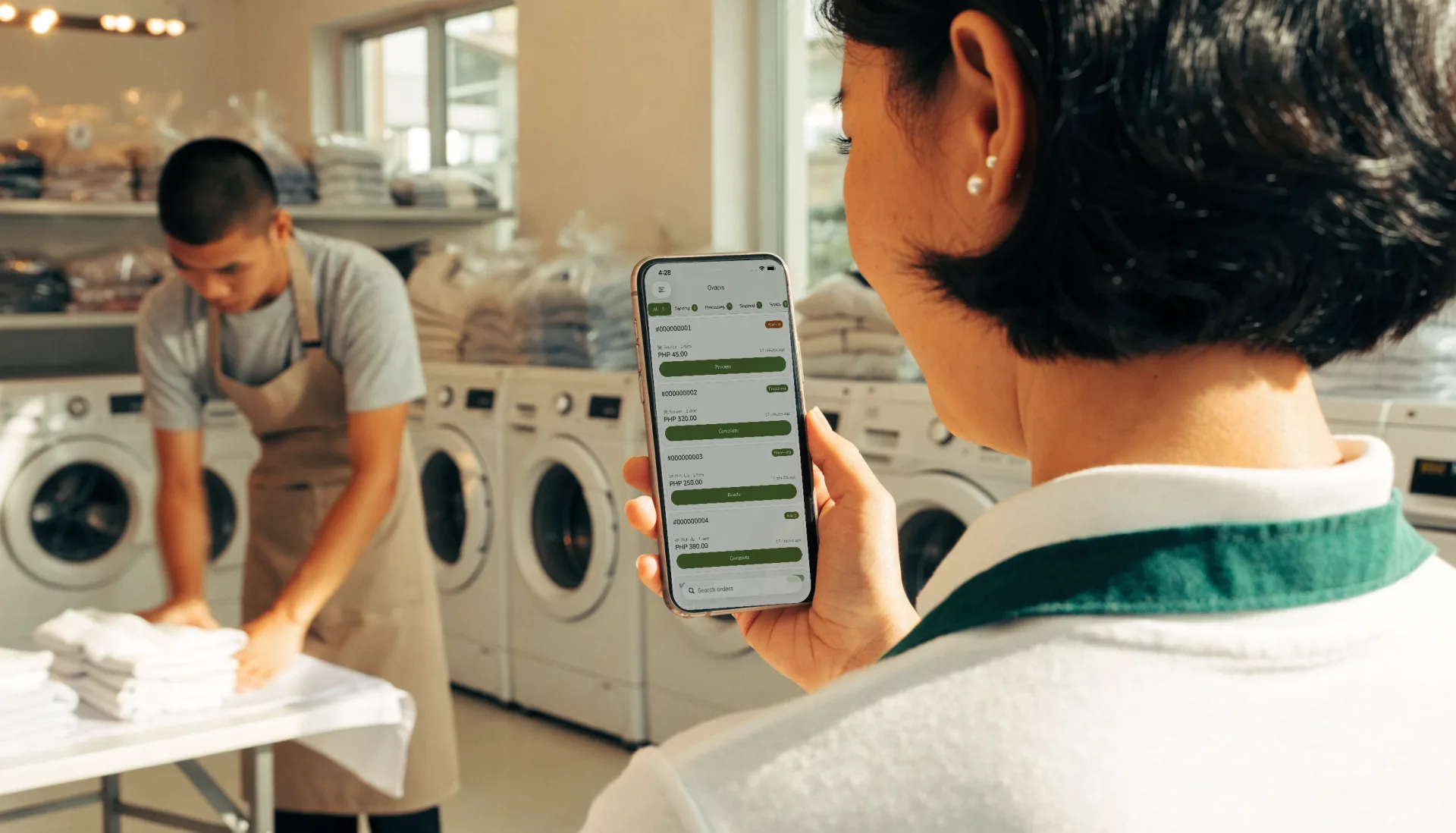 The owner checks the day’s laundry orders by status on Fuze Store on her phone while the washers run and the attendant folds.
