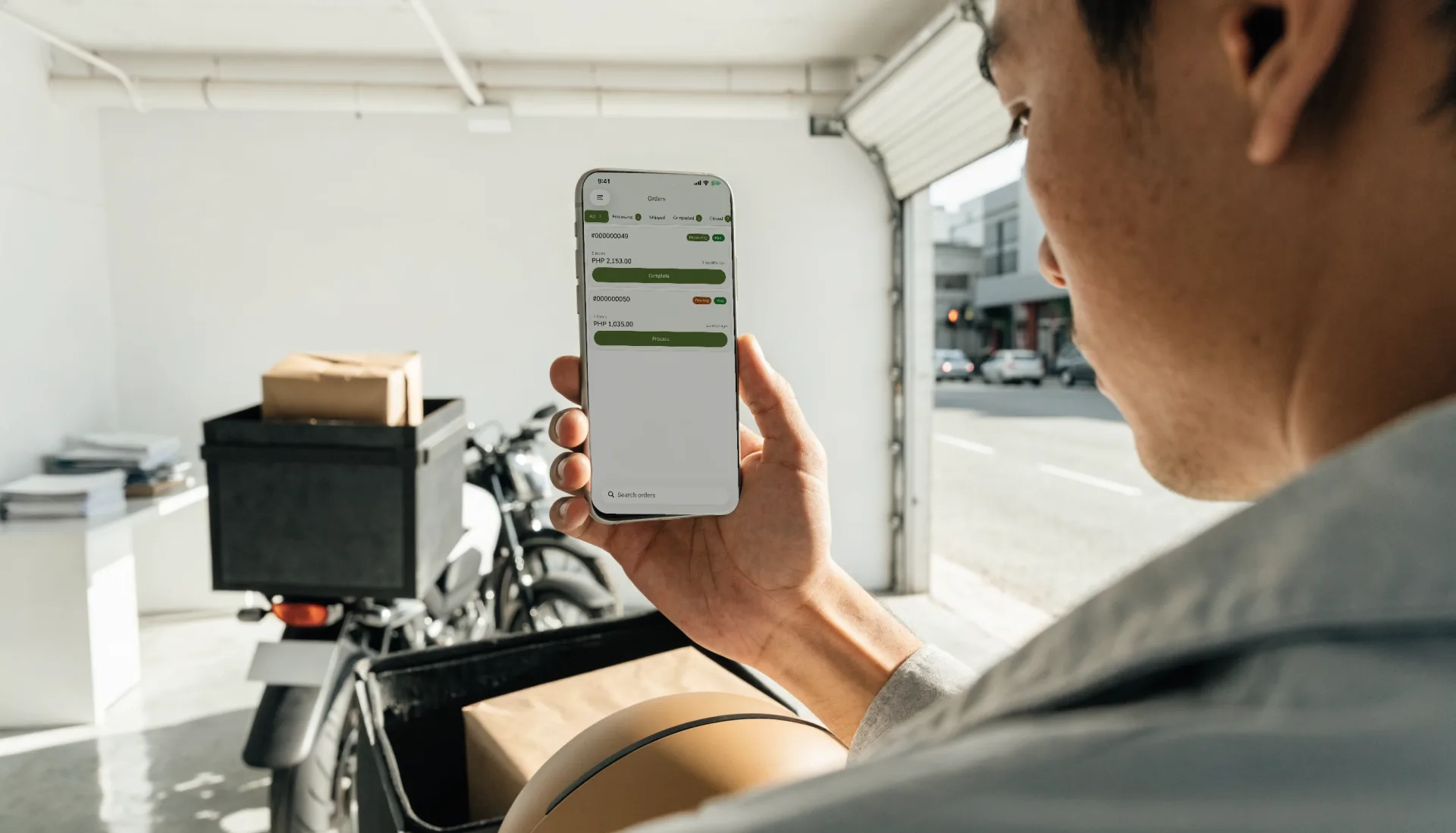 A rider beside his motorcycle checks his orders on Fuze Store on his phone before heading out with a parcel.